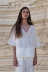 "Model wearing a white unisex linen shirt with a deep V-neckline and wide sleeves, perfect for hot weather.