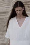 Close-up of the deep V-neckline and wide sleeves of the white unisex linen shirt