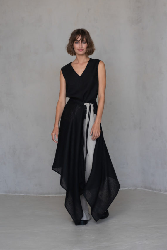 Full-body shot of a model wearing a black linen wrap as a skirt overlay on beige pants.