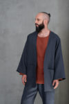 A front view of a men's open-front linen jacket in charcoal gray, showcasing its minimalist design and functional front pockets.